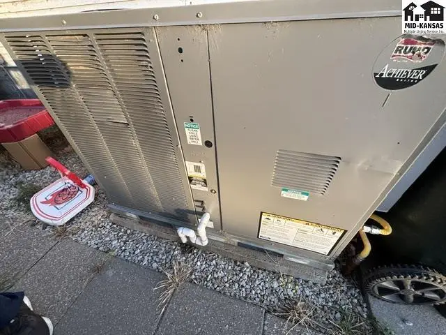 Exterior view of a large, gray central air conditioning unit with visible branding and a small red toy nearby.