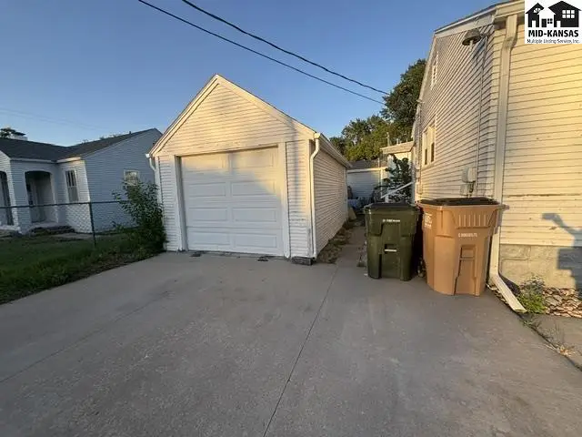 Detached white garage with a white door sits on a concrete driveway next to trash bins.