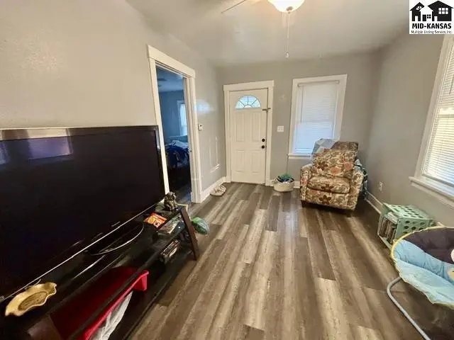 Living room with gray walls, wood-look flooring, a large TV, and a floral armchair.