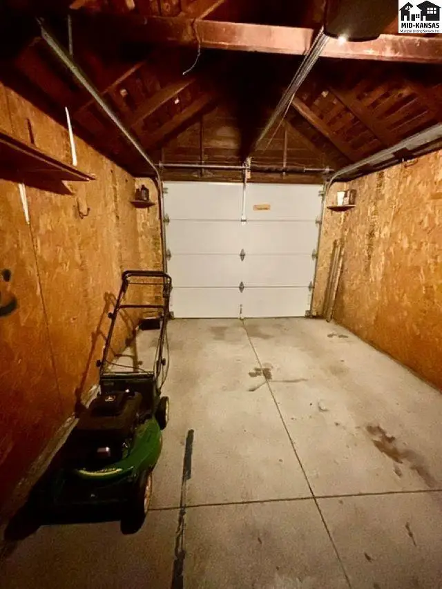 Interior of a two-car garage with plywood walls, concrete floor, and a white overhead door.