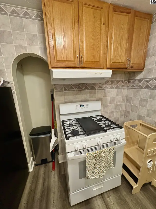 White gas range with a griddle top sits beneath wood cabinets and a tiled backsplash.