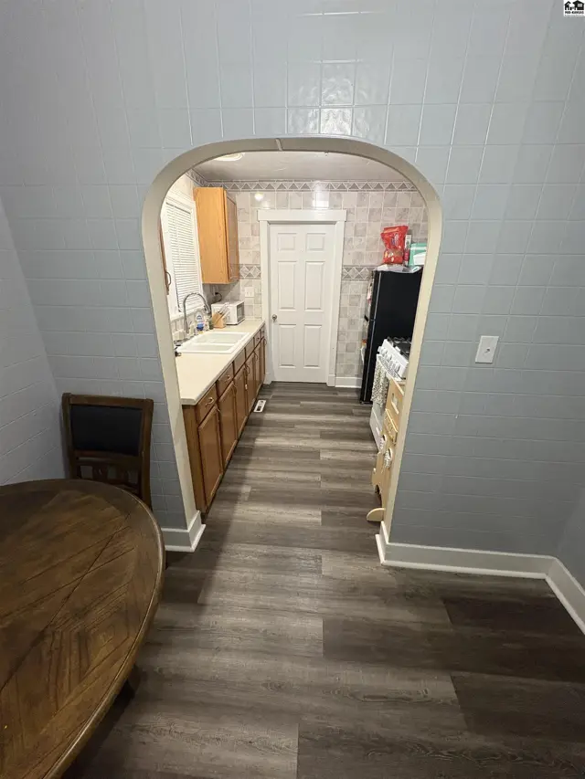 An arched doorway opens to a kitchen with wood cabinets, a white sink, and a black refrigerator.