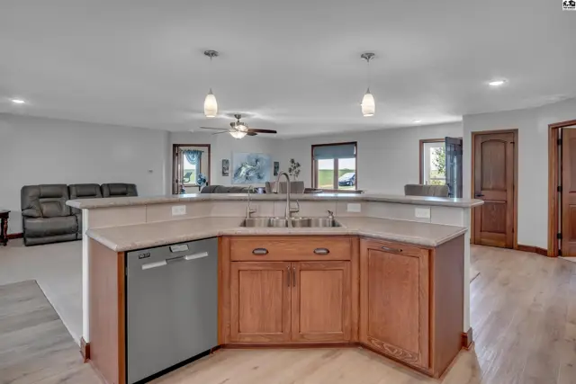 Spacious kitchen with light wood cabinets, granite countertops, and stainless steel appliances opens to a living area.
