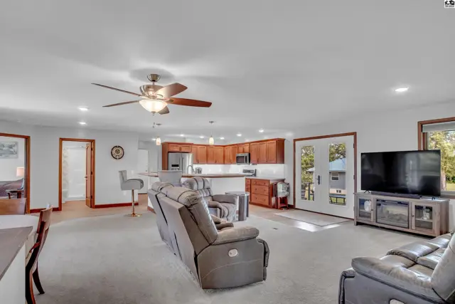 Spacious living room with plush recliners, a modern kitchen with wood cabinets, and a ceiling fan.