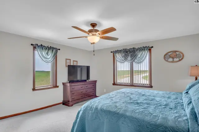 Spacious bedroom with a large bed, dresser, TV, ceiling fan, and scenic countryside views.