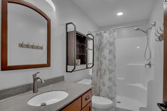 Modern bathroom with a gray vanity, white sink, wood cabinets, and a white shower with a floral curtain.