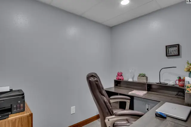 A home office with gray walls, a dark wood desk, and a leather office chair.