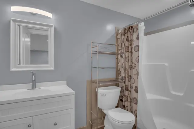 Modern bathroom with white vanity, gray walls, and a seashell-patterned shower curtain.