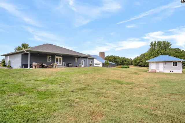 Spacious gray ranch home with blue accents and a detached garage sits on a large, grassy lot.