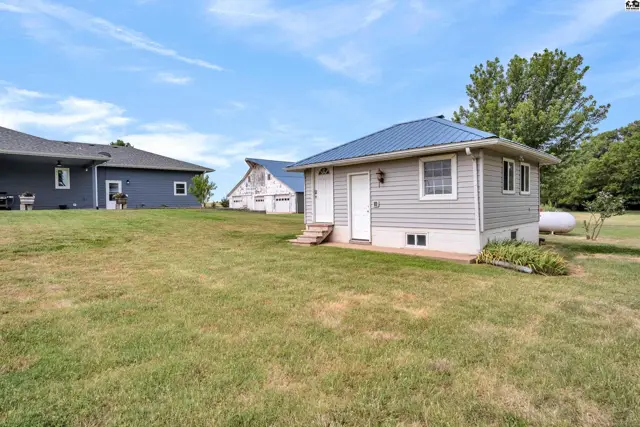 Gray vinyl-sided outbuilding with a blue metal roof sits on a grassy lawn.