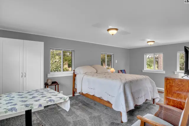 Spacious bedroom with a white-quilted bed, gray walls, large windows, and a white wardrobe.