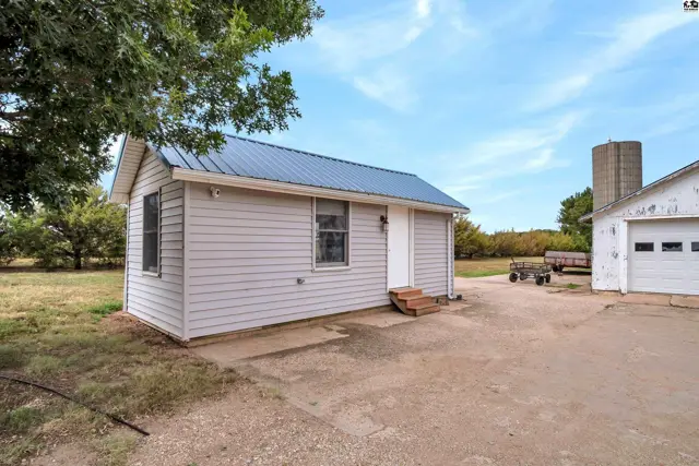 Small gray vinyl-sided building with a blue metal roof and a white garage door nearby.