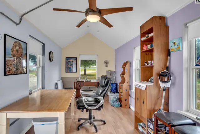 Bright room with light wood floors, vaulted ceiling, and a large wooden hutch filled with items.