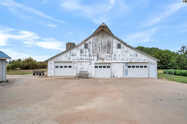Expansive white barn with peeling paint and three garage doors sits on a concrete pad.