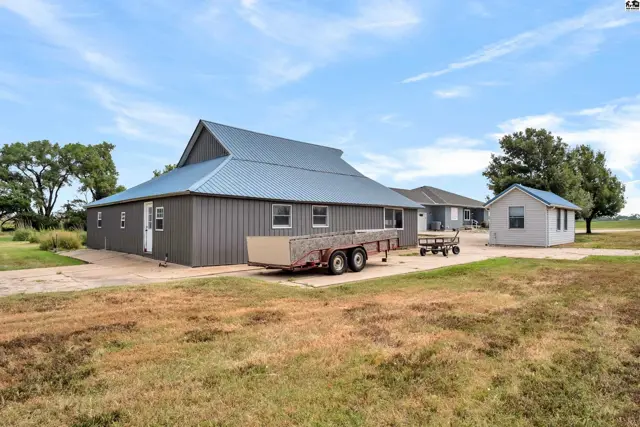 Gray metal-sided building with a blue metal roof, featuring a trailer and a small detached shed.