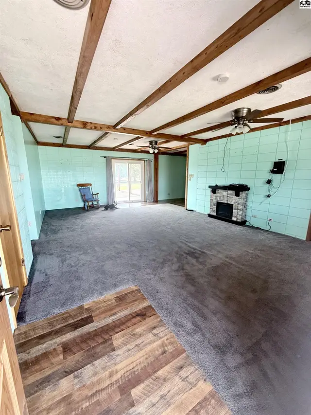 Spacious living area with carpet, wood-beamed ceiling, and stone fireplace.