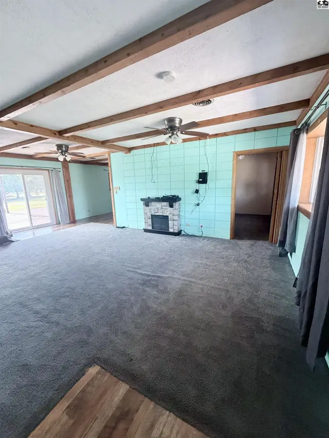 Spacious living area with carpet, wood-beamed ceiling, and a stone fireplace.
