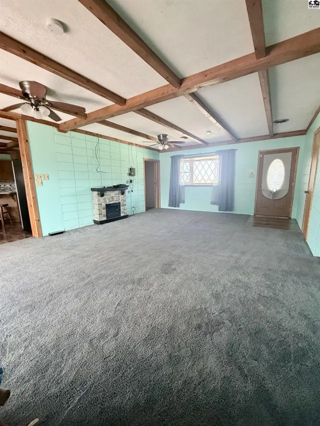 Spacious living room with carpet, fireplace, wood-beamed ceiling, and ceiling fans.