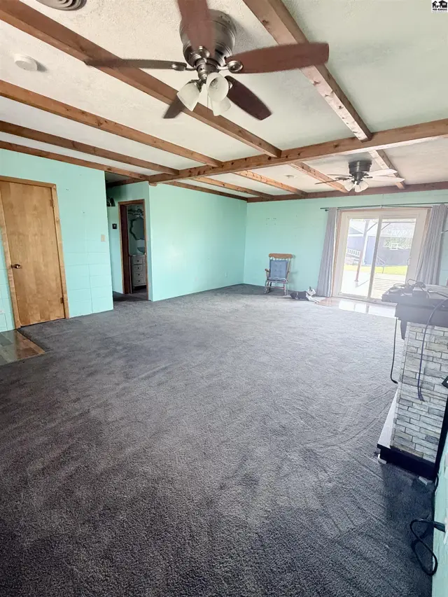 Spacious living area with carpet, wood-beamed ceiling, and stone fireplace.