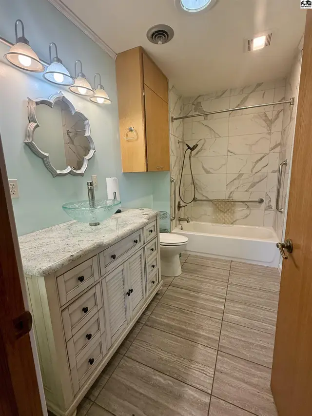 This bathroom features a vanity with a granite countertop, a glass vessel sink, and a tiled shower-tub combination.