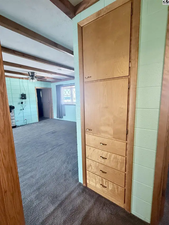 A tall wooden cabinet with drawers stands against a mint green tiled wall.