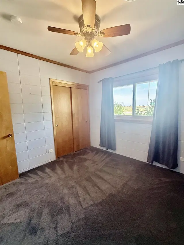 Carpeted room with a ceiling fan, closet, and large window with curtains.