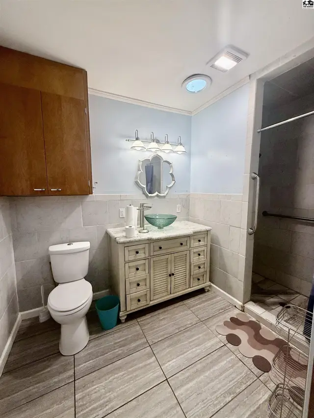 This bathroom features a vanity with a vessel sink, a toilet, and a walk-in shower.