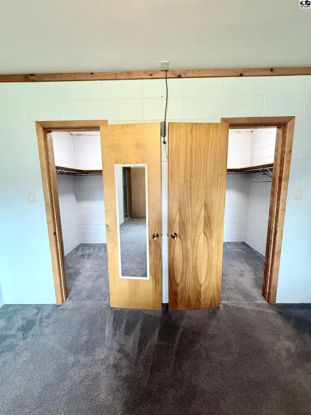 Two open wooden doors reveal white-tiled closets with shelving and hanging rods.