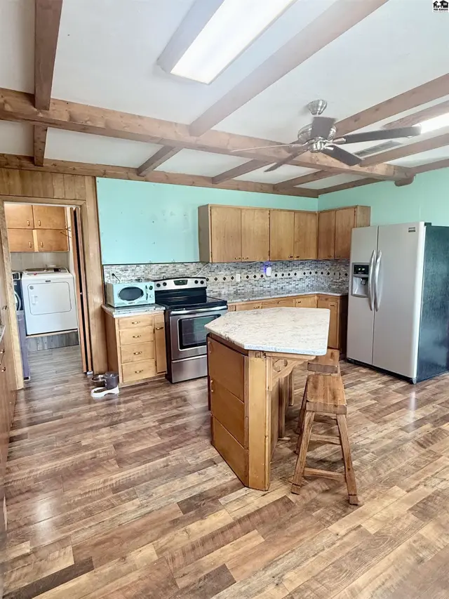 This kitchen features wood cabinetry, a central island, stainless steel appliances, and wood-look flooring.