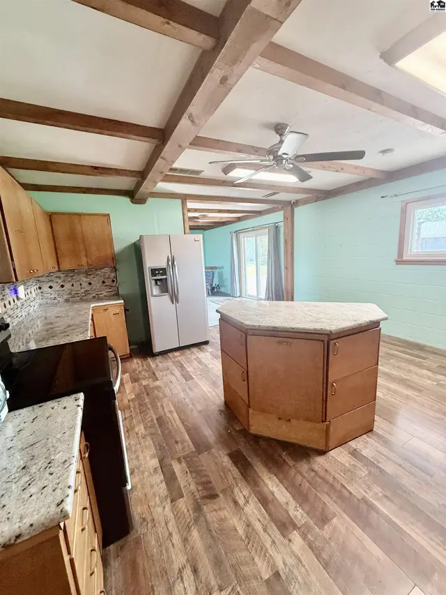 Kitchen features wood cabinetry, granite countertops, a central island, and a ceiling fan.