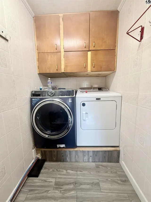 This laundry area features a front-loading washer, a top-loading dryer, and overhead wood cabinetry.