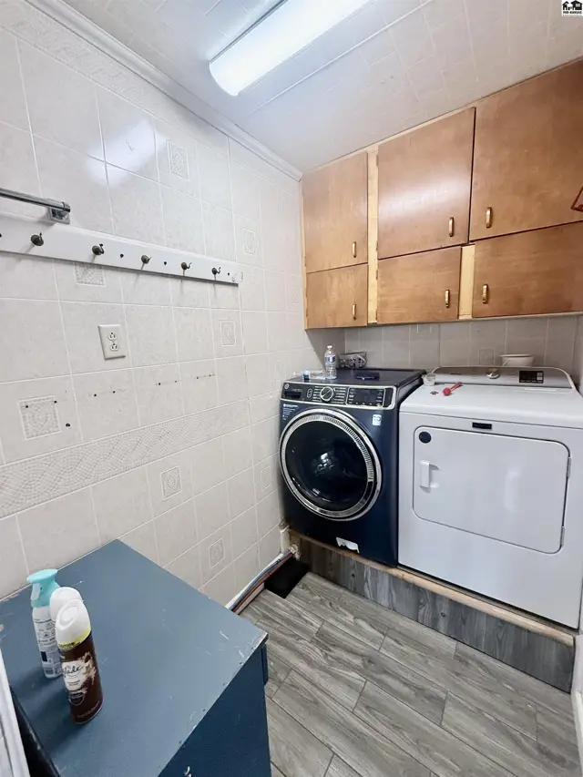 This laundry room features tile walls, wood cabinetry, a washer, and a dryer.
