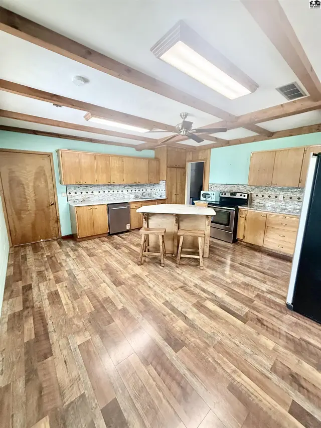 Spacious kitchen features wood cabinetry, a central island with seating, and wood-look flooring.