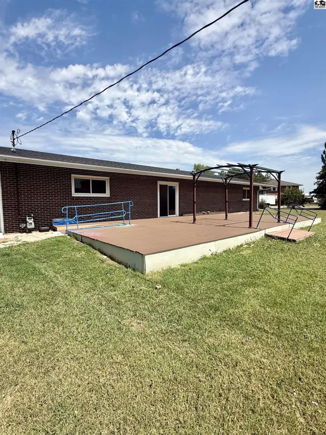 A large, elevated deck with a metal pergola extends from the brick home.