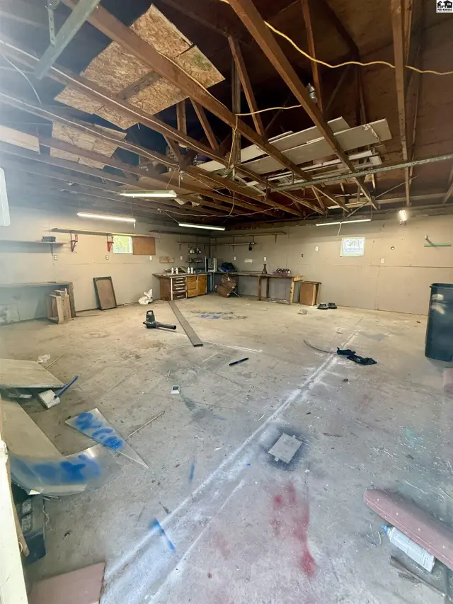 Spacious unfinished room with concrete floor, exposed ceiling beams, and workbenches.