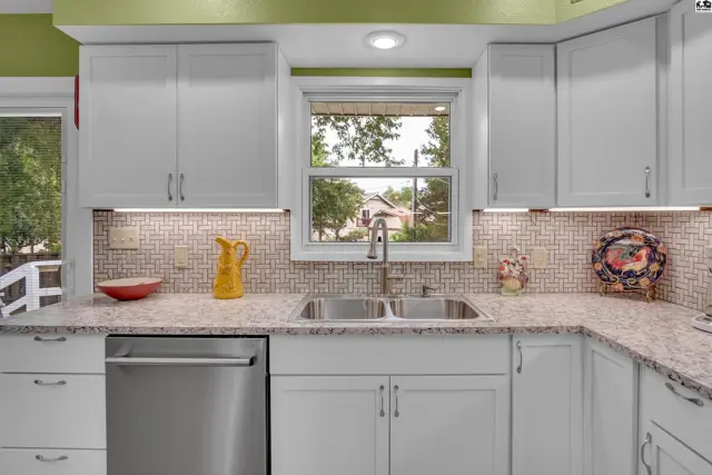 White cabinetry, granite countertops, and a mosaic tile backsplash accent this kitchen.