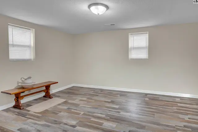 Spacious room with two windows, wood-look flooring, and a wooden bench.