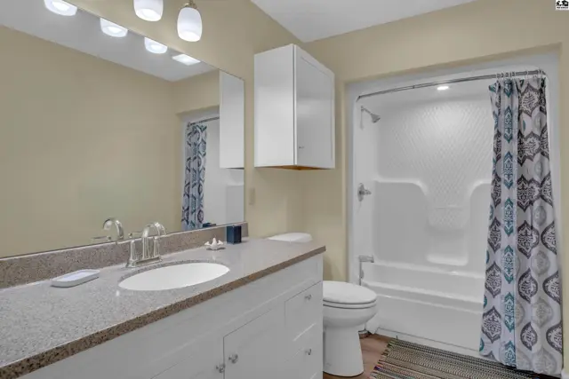 This bathroom features a white vanity, granite countertop, toilet, and a shower-tub combination.