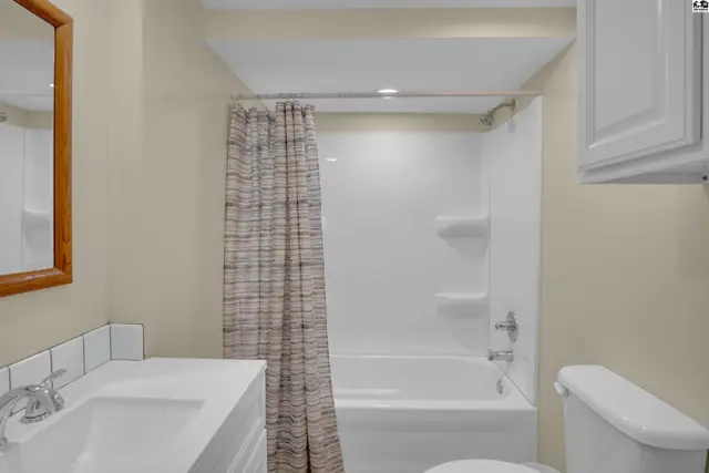 This bathroom features a white vanity, toilet, and bathtub with a patterned shower curtain.
