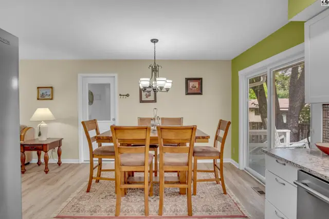 A dining area with a wooden table, chairs, and a chandelier is adjacent to a sliding glass door.