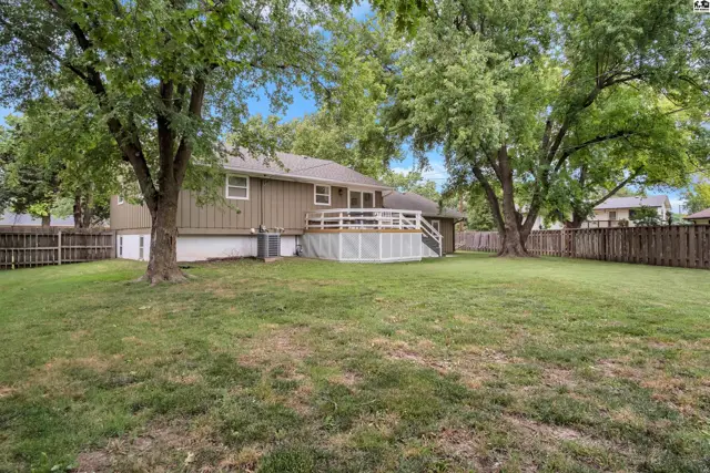 A wooden deck with white railings overlooks a grassy backyard surrounded by mature trees.