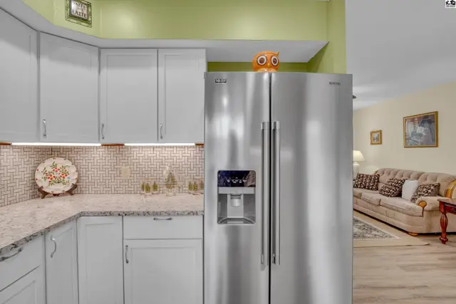 Stainless steel refrigerator stands in a kitchen with white cabinets and granite countertops.