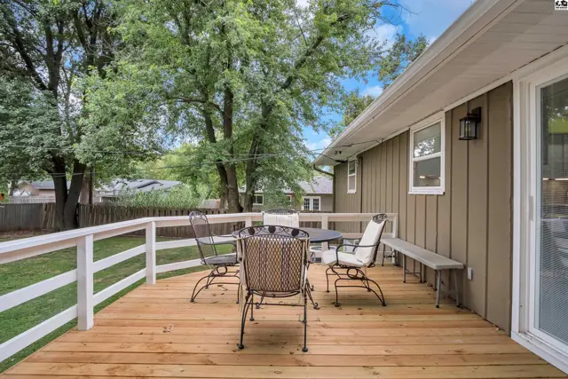 Wooden deck with white railing, outdoor seating, and a bench overlooks a grassy yard.