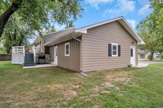 Exterior features tan siding, white trim, a deck, and a concrete driveway.