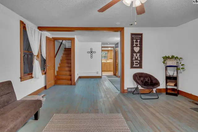 Living room features light blue painted wood floors, a ceiling fan, and an open doorway to a staircase.