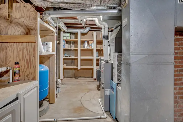 This unfinished basement features concrete floors, exposed pipes, and storage shelving.