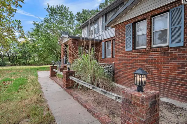 Brick home with a covered porch, mature trees, and a paved walkway.