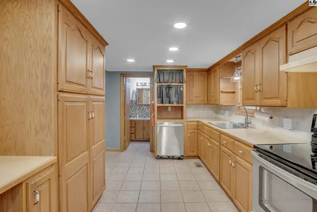 Spacious kitchen features light wood cabinetry, tiled floors, and ample counter space.