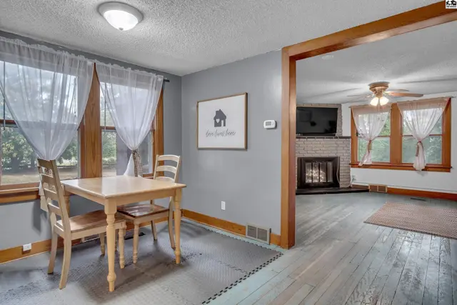A dining area with a wooden table and chairs opens to a living room with a fireplace.