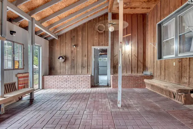 Covered patio with brick flooring, wood paneling, and built-in seating.